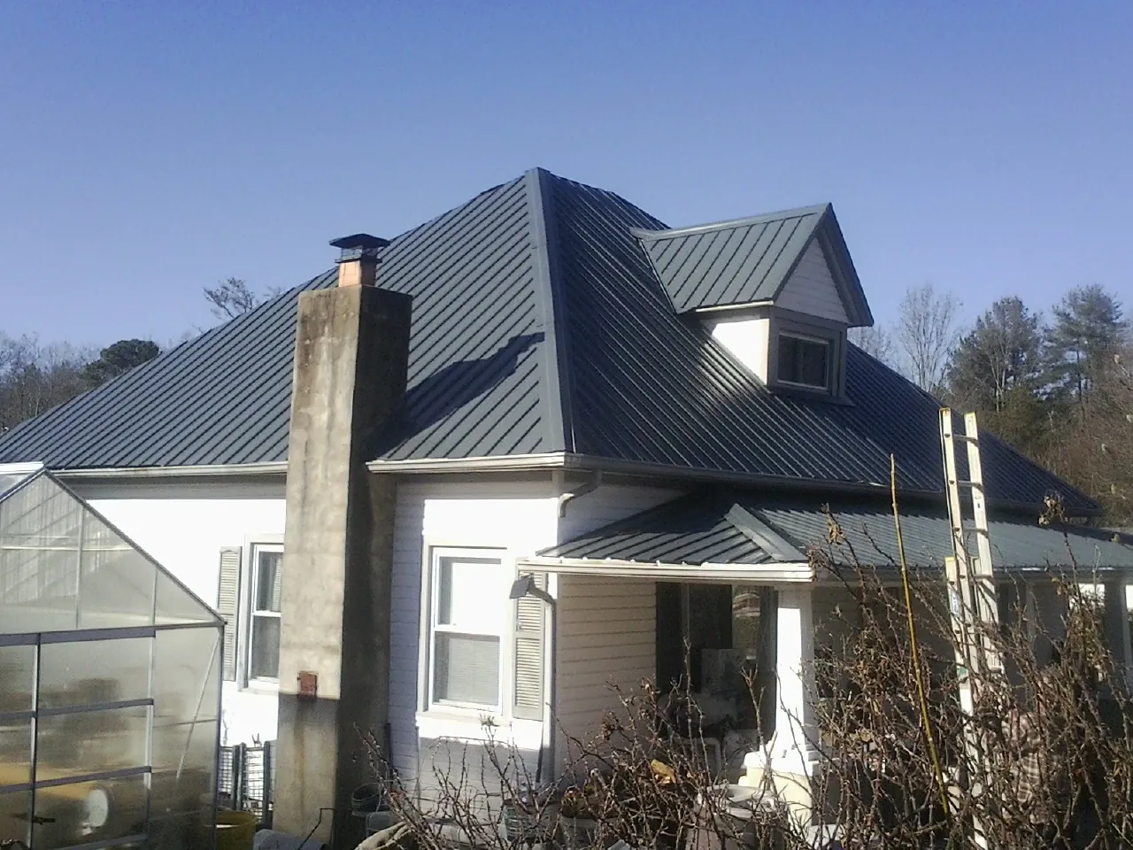 Dark blue standing seam metal roof on a white farmhouse with dormer — Slate & Tile Roof Repair by Roofing Brothers in Mingo