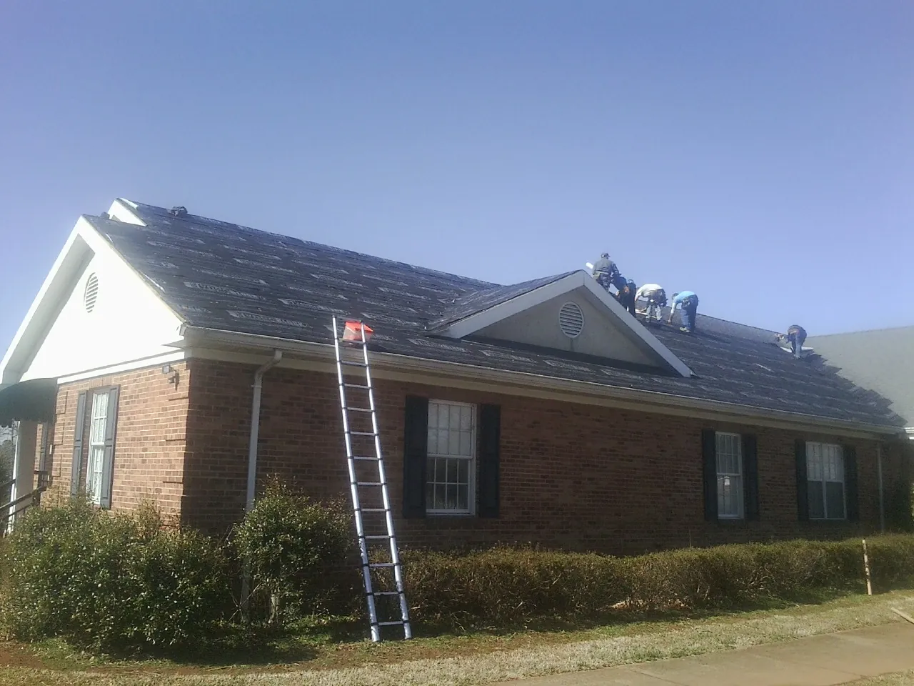 Crew tearing shingles off a brick ranch roof with a ladder set — Emergency Roof Repair work by our crew in Mingo