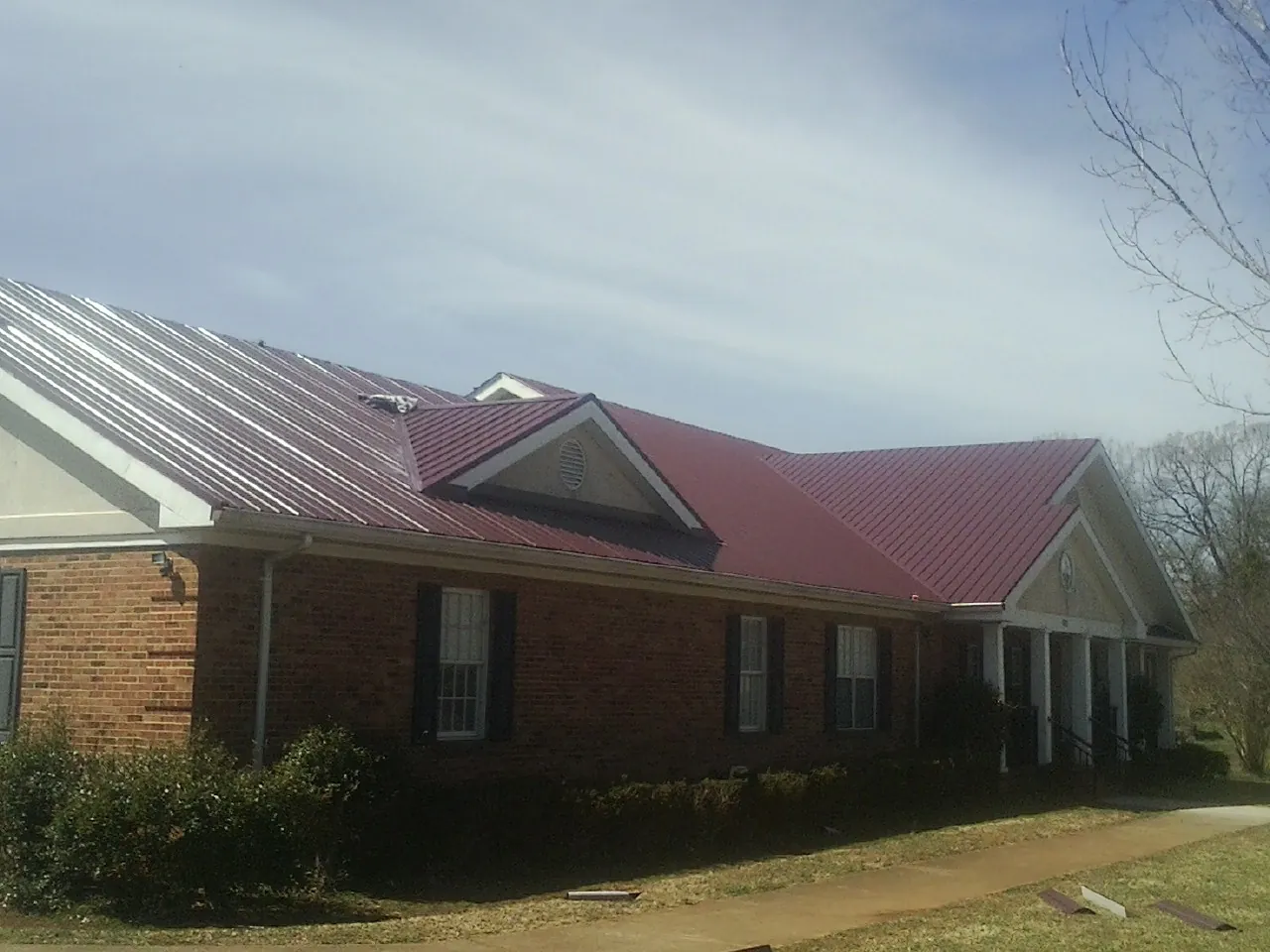 Red metal roof with gabled entries on a long brick building, from a Hail Damage Roof Repair job in Mingo