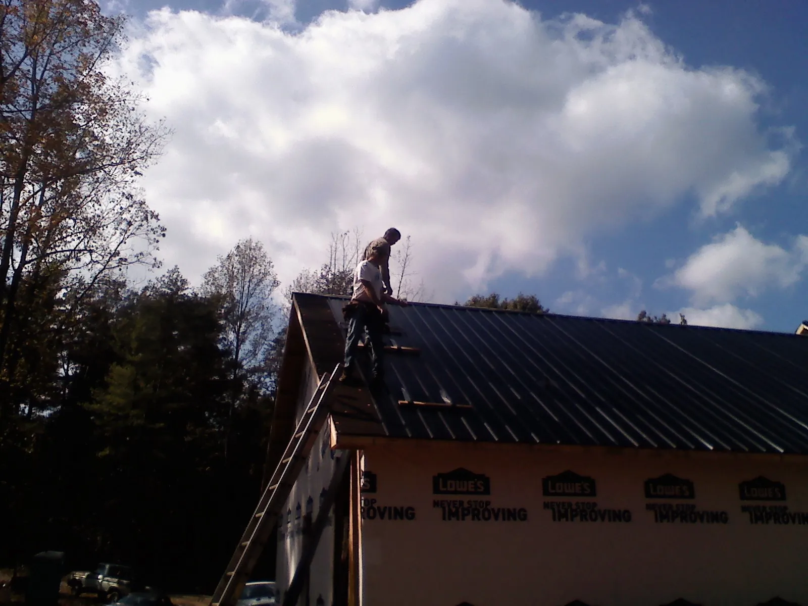 Roofer fastening dark metal panels high against a cloudy sky, from a Roof Inspection job in Mingo