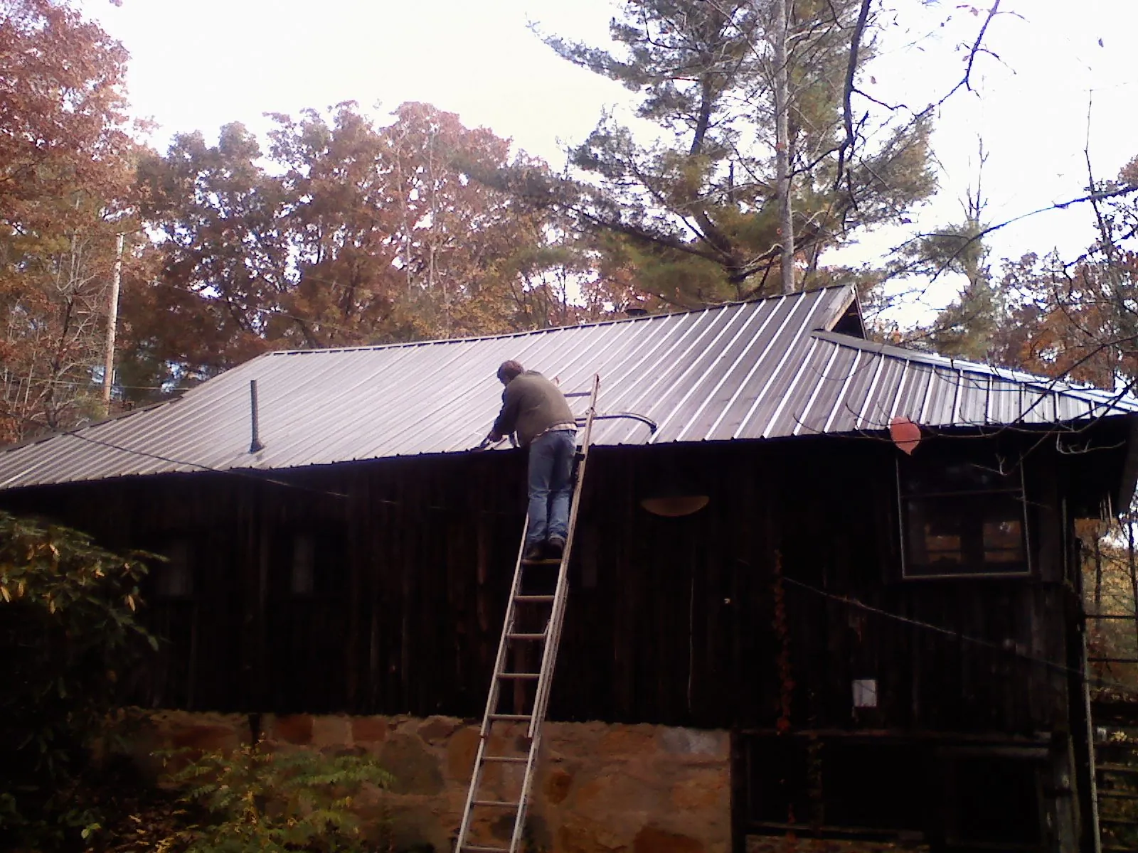 Roofer on a ladder working along the edge of a cabin metal roof in Mingo