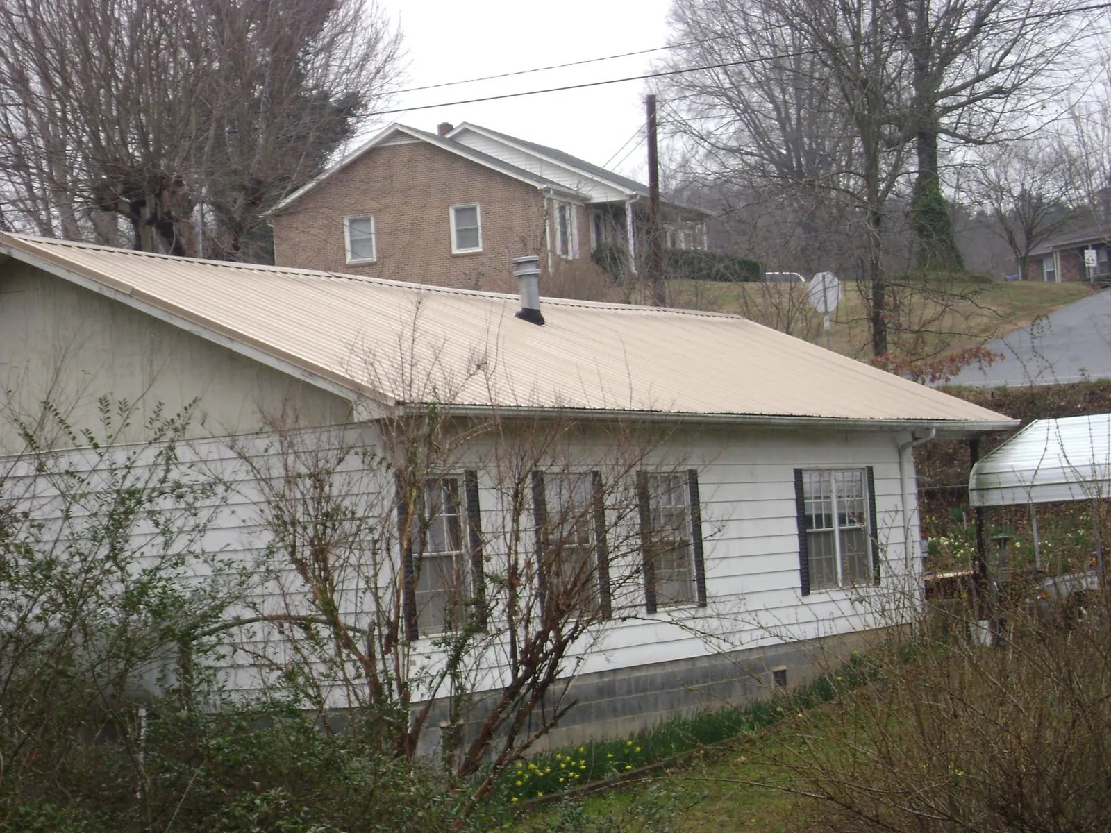 Tan metal roof on a white sided house set into a hillside — Commercial Roofing by Roofing Brothers in Mingo