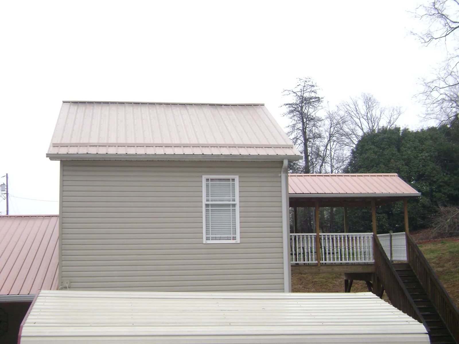 Tan metal roofs on a two story addition and attached porch, from a Roof Replacement job in Mingo